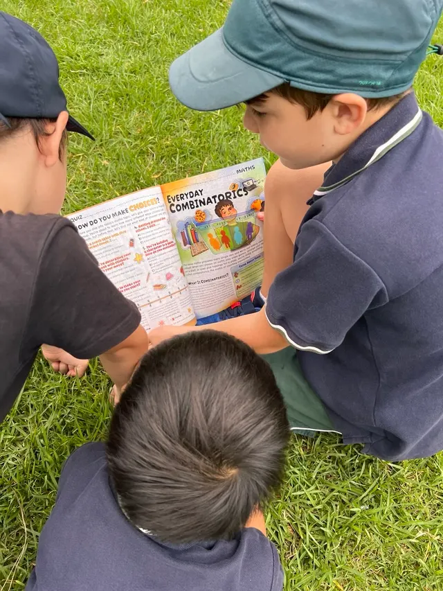 Three children exploring an OYLA Junior article together on the grass.