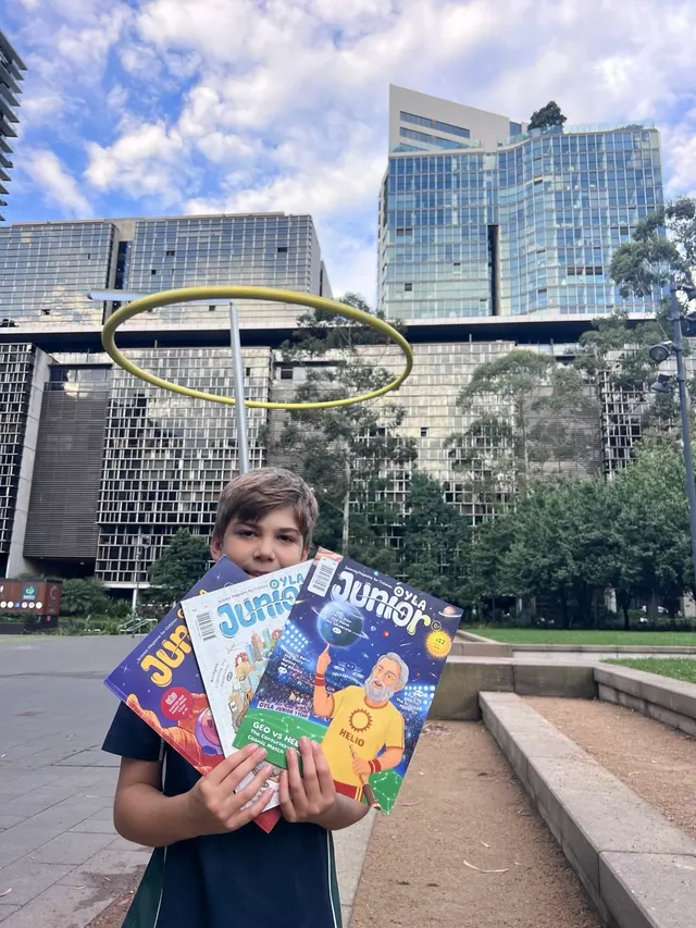 A young reader holding three colorful issues of OYLA Junior.