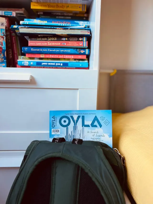 An OYLA magazine tucked into a school backpack beside a bookshelf.