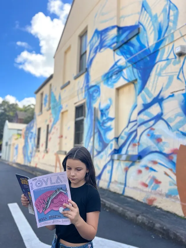 A reader absorbed in OYLA beside a colorful mural.