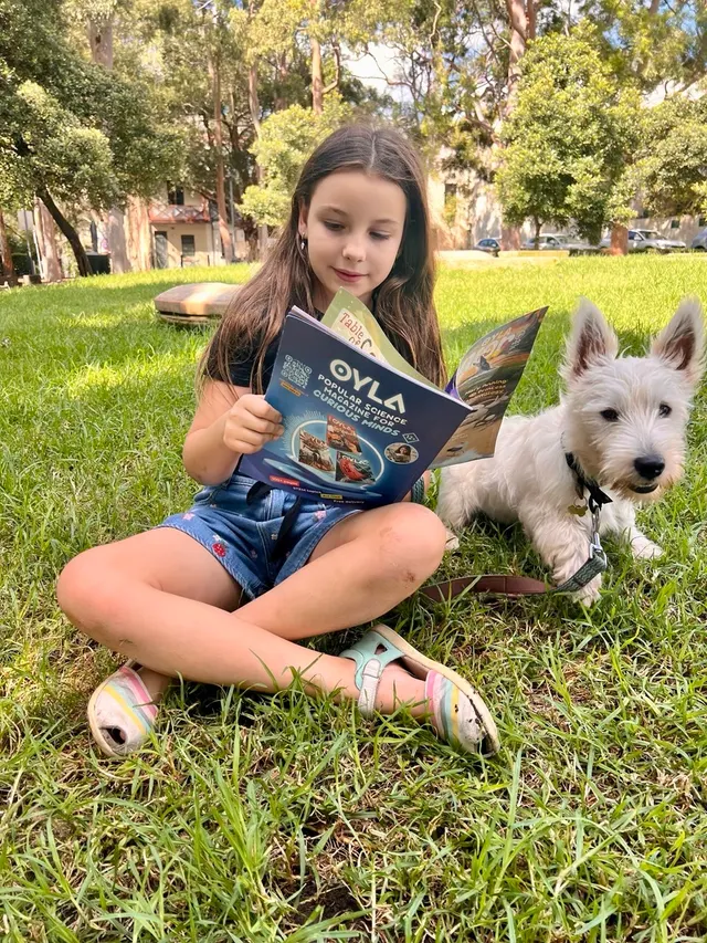 A reader enjoying OYLA on the grass beside a white dog.
