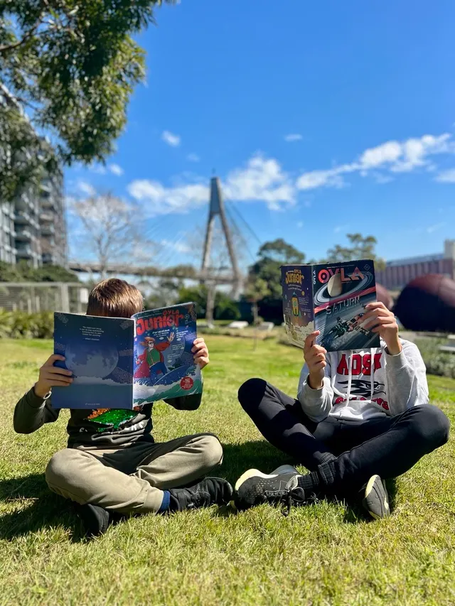 Two children reading OYLA Junior and OYLA Magazine together in a park.