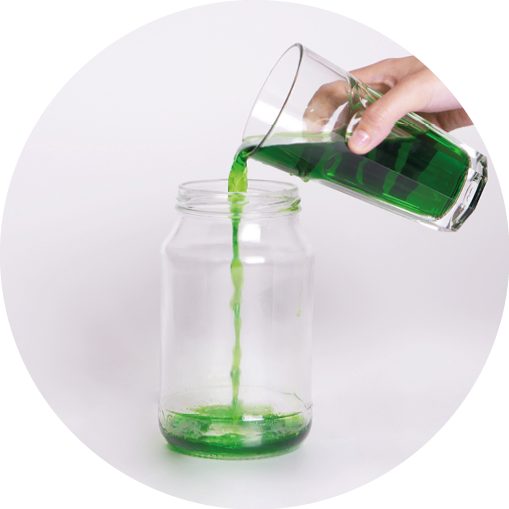 A person pouring green liquid into a glass jar to create a homemade lava lamp.