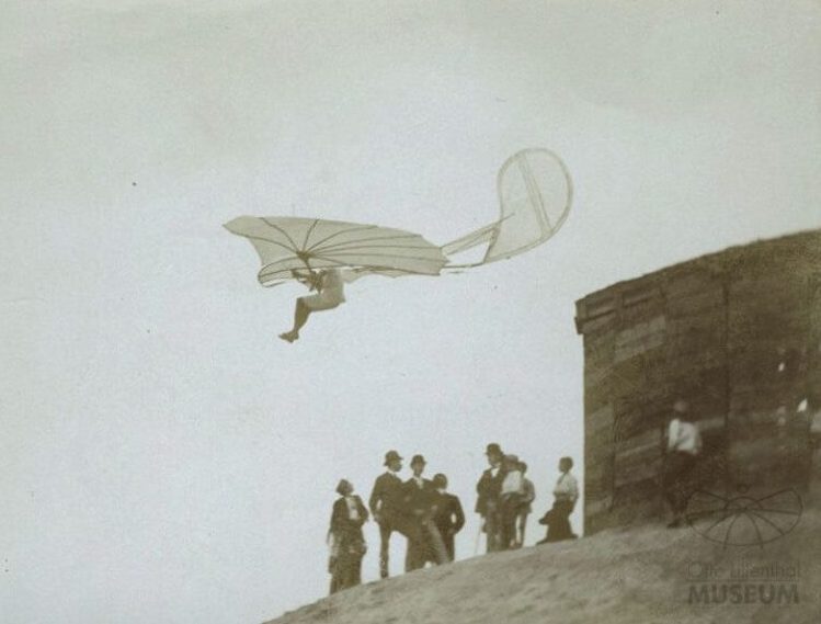 An old photo of a man paragliding over a hill.