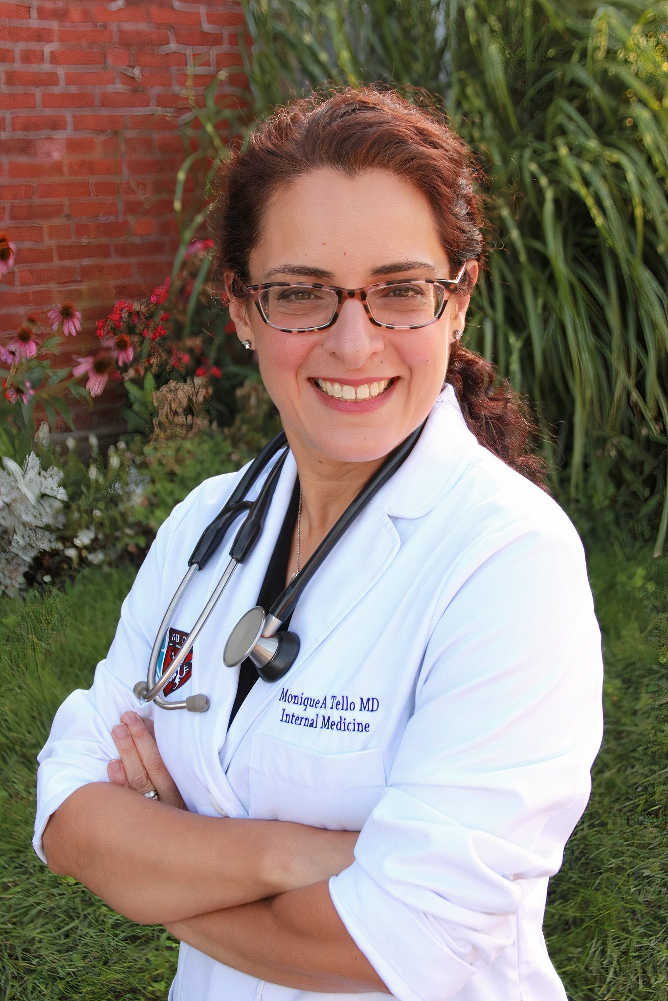 A woman in a white coat standing in front of a brick wall.