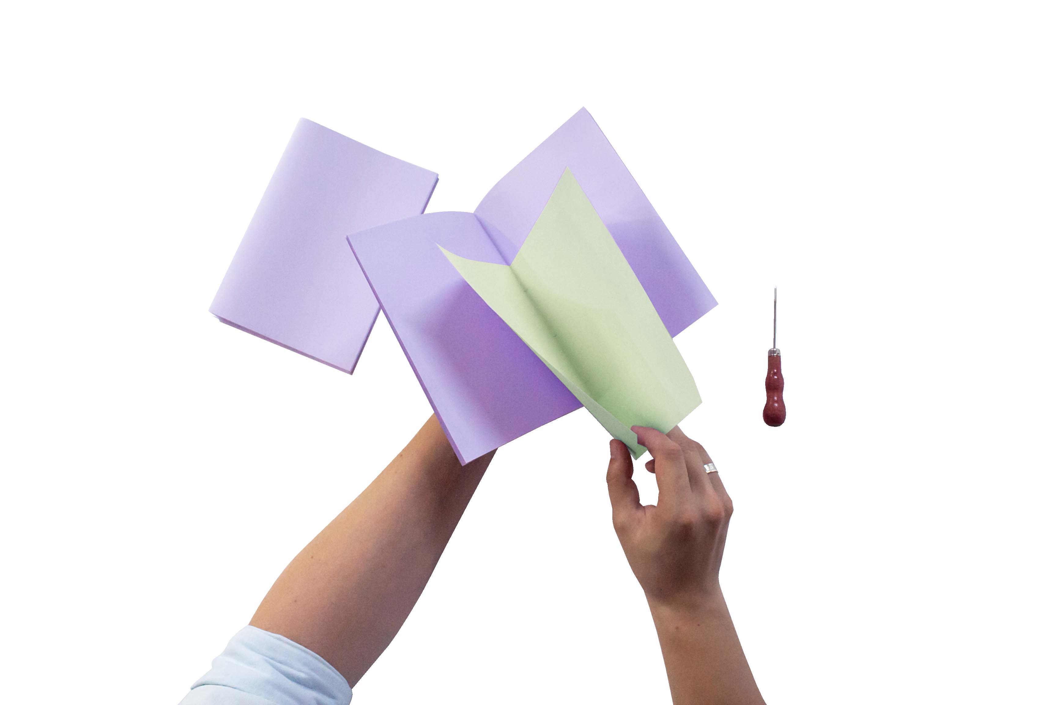 Bookbinding. Hands holding assorted colored paper and a small screwdriver against a white background.