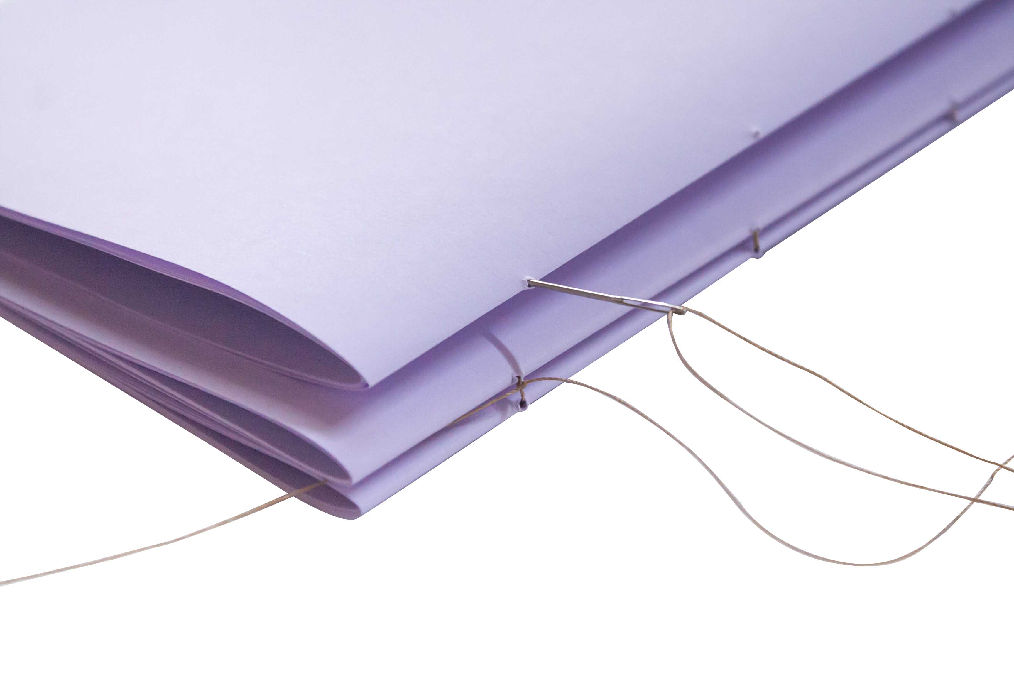Bookbinding. A stack of purple paper bound by a needle and thread.