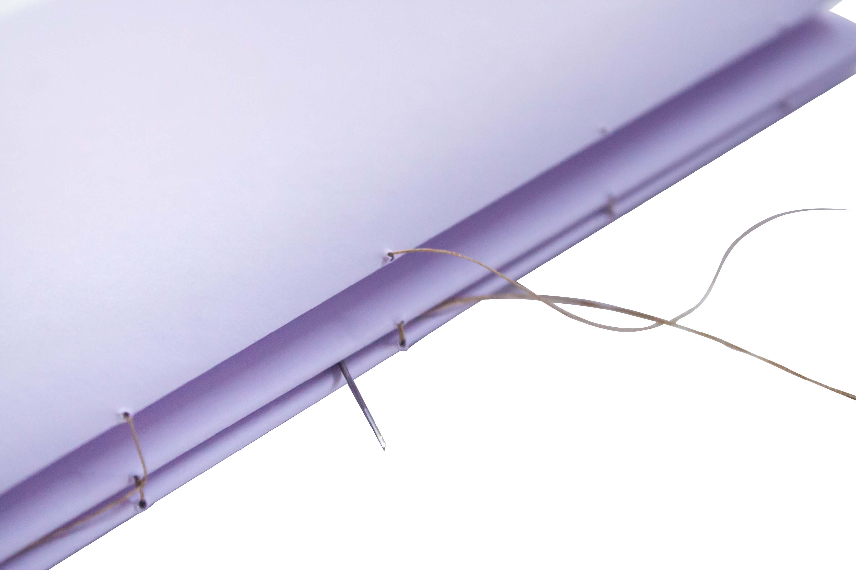 A needle with thread passing through holes along the edge of a purple material.