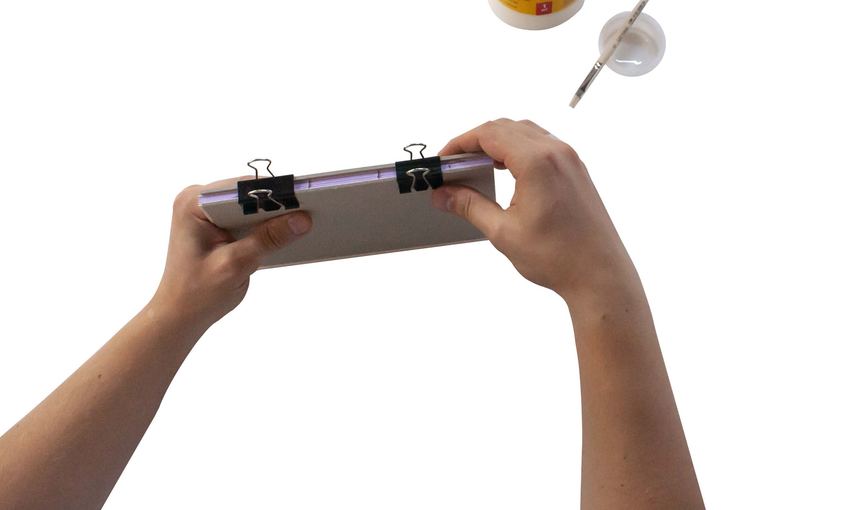 Hands holding a clipboard with blank paper, with a cup of coffee and a spoon nearby on a white surface.
