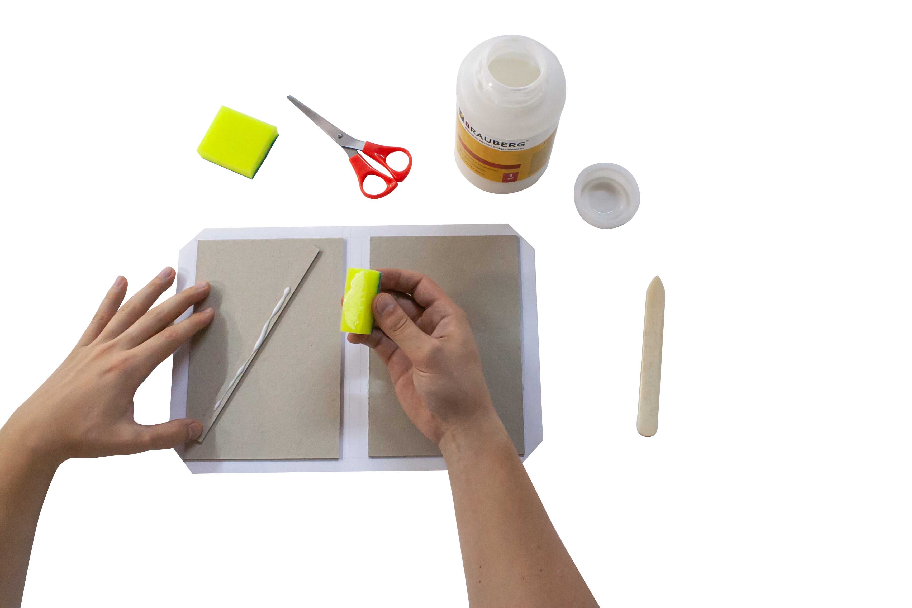 Person applying glue to a sponge for a craft project, with scissors, glue, and additional sponges on a table.
