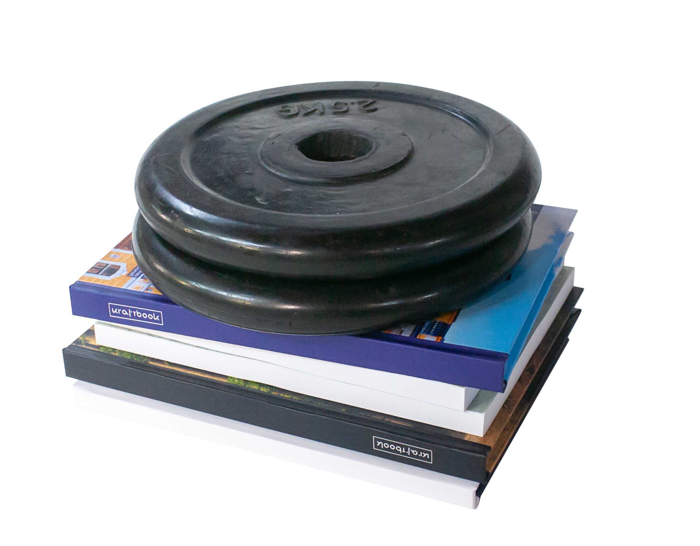 Bookbinding. A stack of books topped with a 20 kg weight plate.